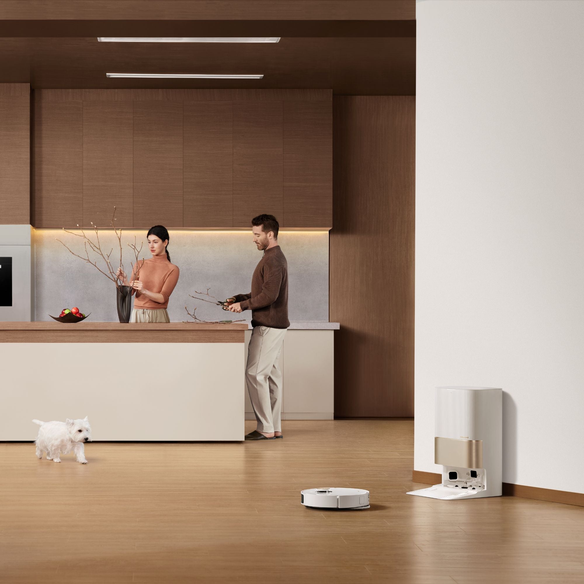 Couple enjoying a modern kitchen while a Dreame robot vacuum cleans nearby, with pet-friendly features and automatic docking station.